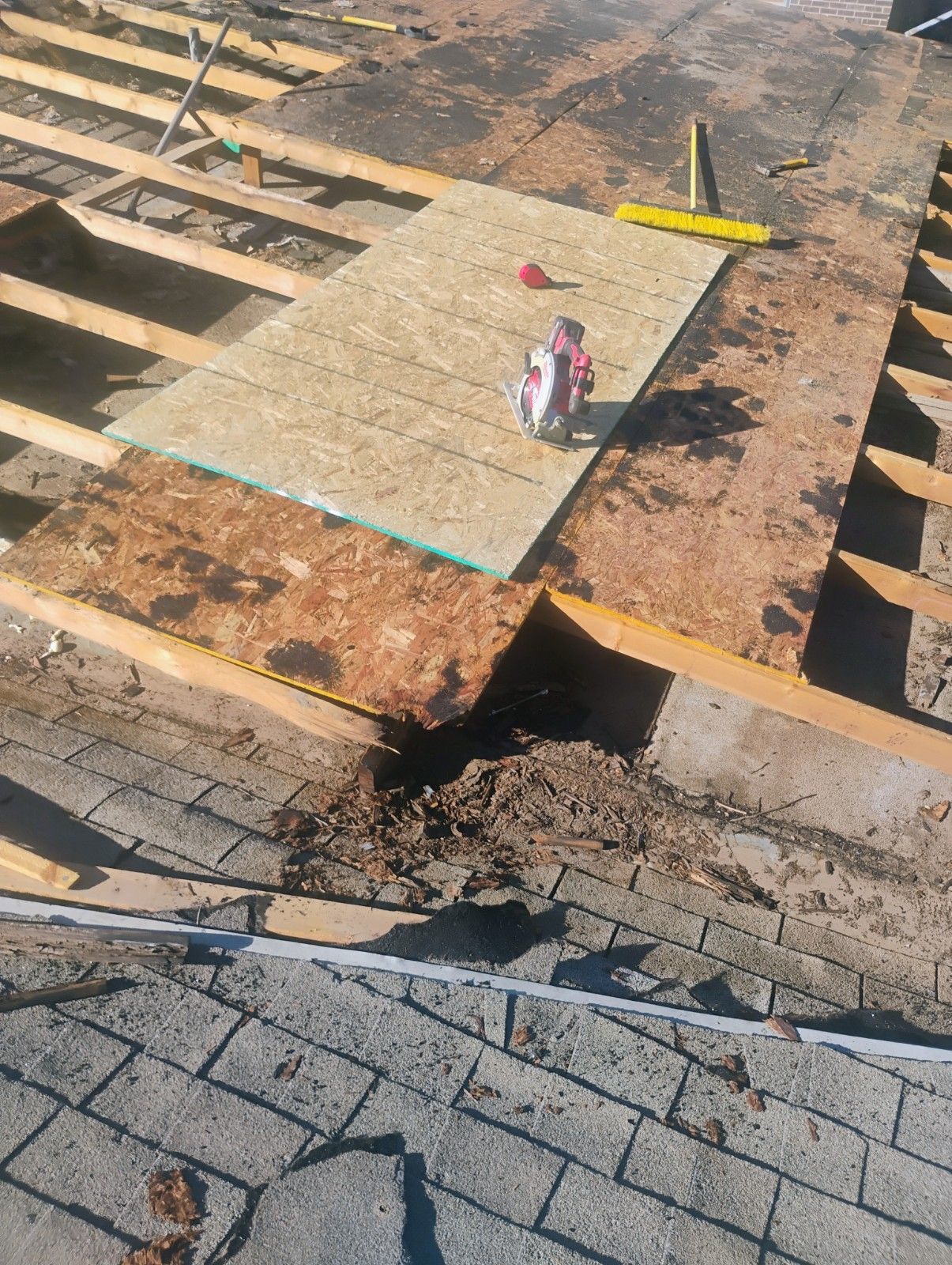 Roof under construction, showing exposed rafters, plywood, and a circular saw.