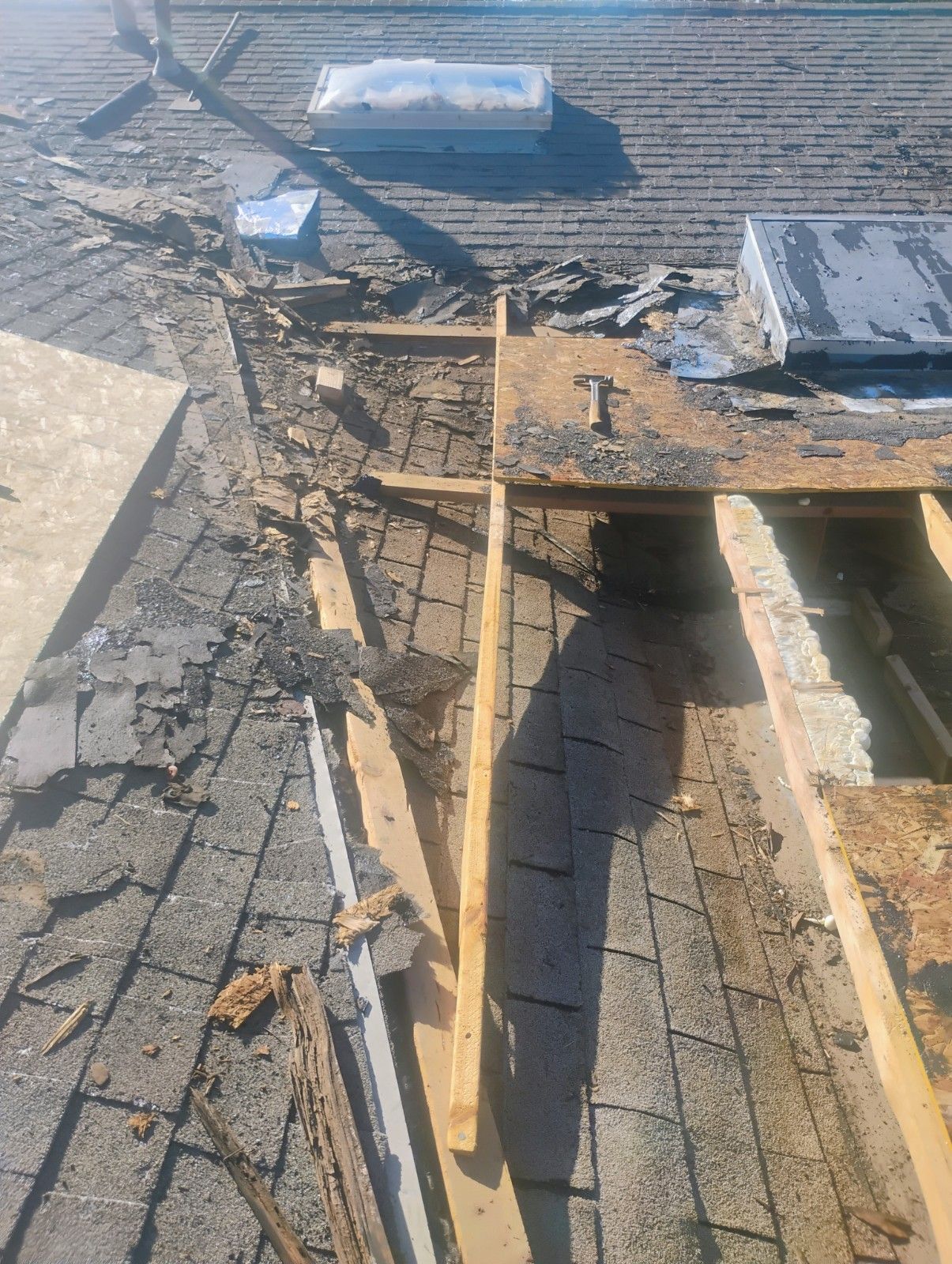 Roof partially torn apart, revealing wooden beams and mesh, near a skylight.