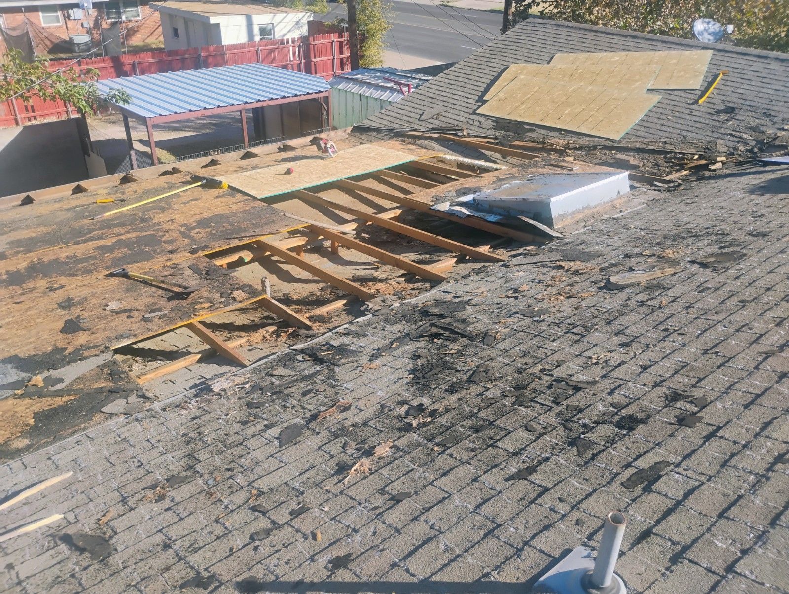 Roof partially torn off, revealing wooden supports. Debris and exposed underlayment visible. Outdoors in daylight.
