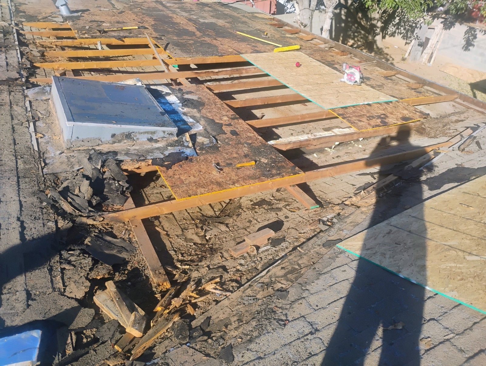Roofing project: Debris, exposed beams, partially removed roof, metal box, and person's shadow.