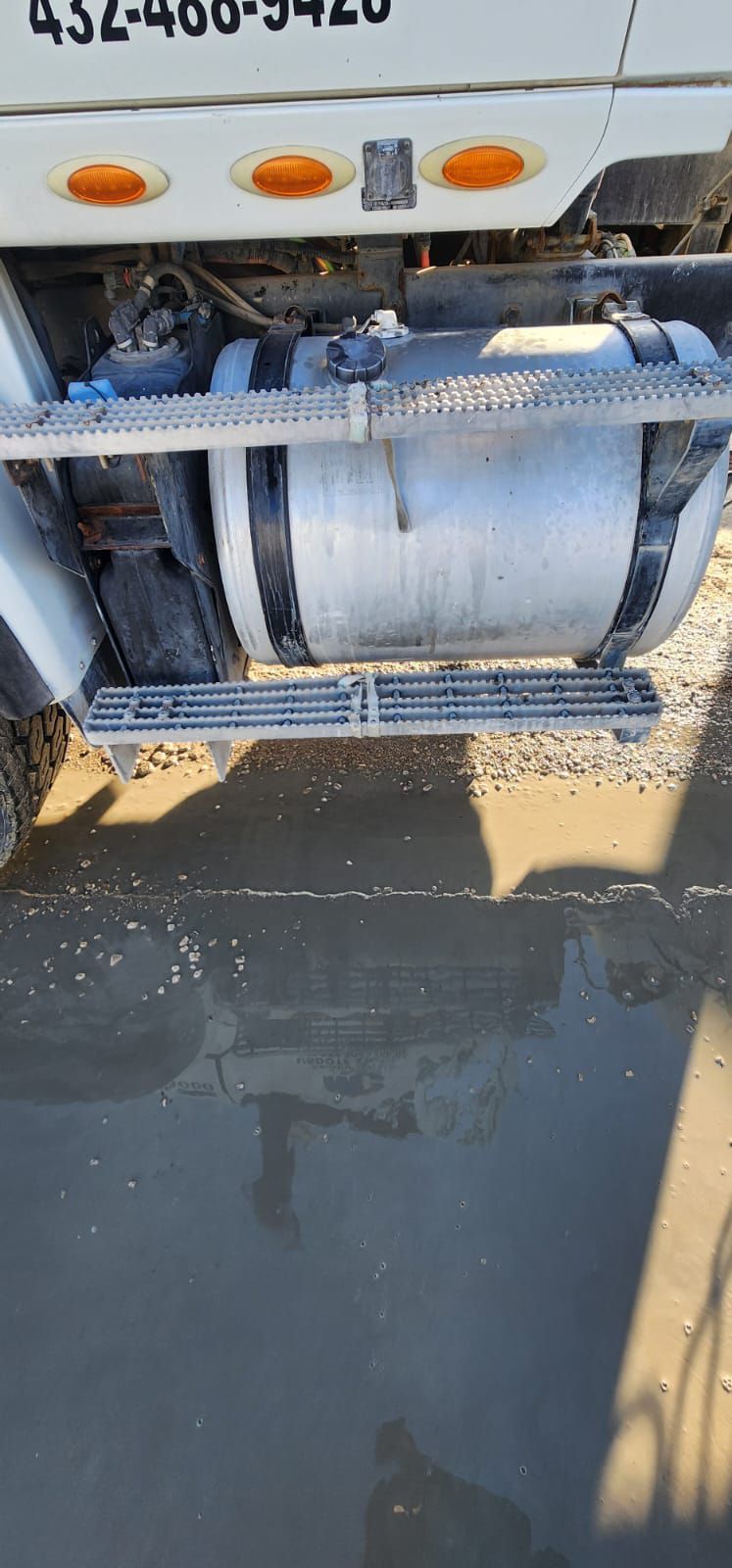 A truck's fuel tank and step are seen above muddy ground.