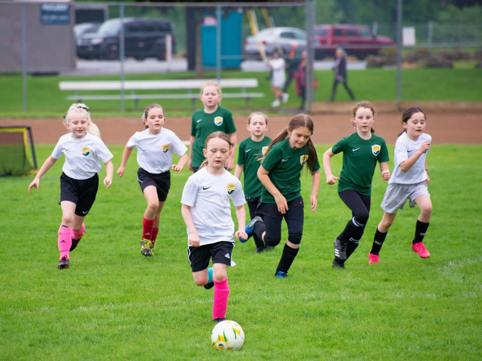 Young soccer players running on a green field towards the camera, some wearing white shirts, others green.