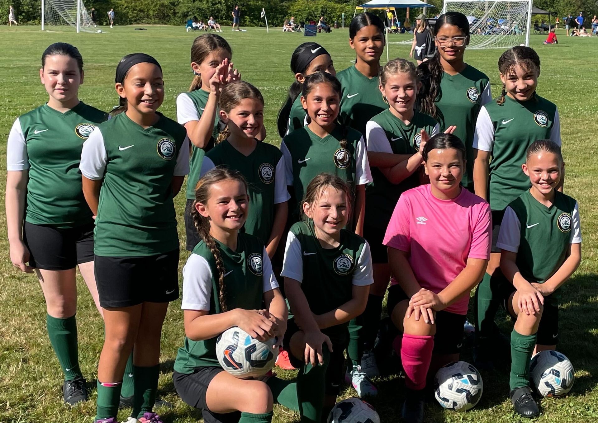 Soccer team in green jerseys poses on a field, some kneeling with soccer balls.