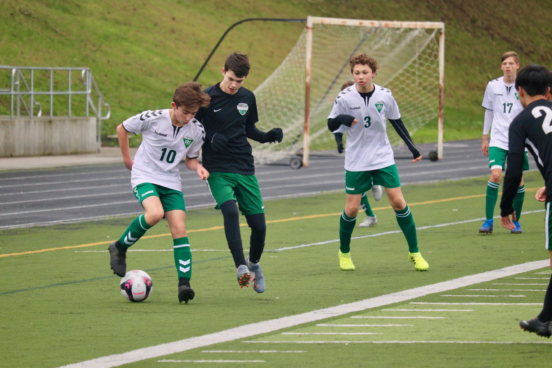 Soccer players on a field. One dribbles, two others wait. Green and white jerseys.