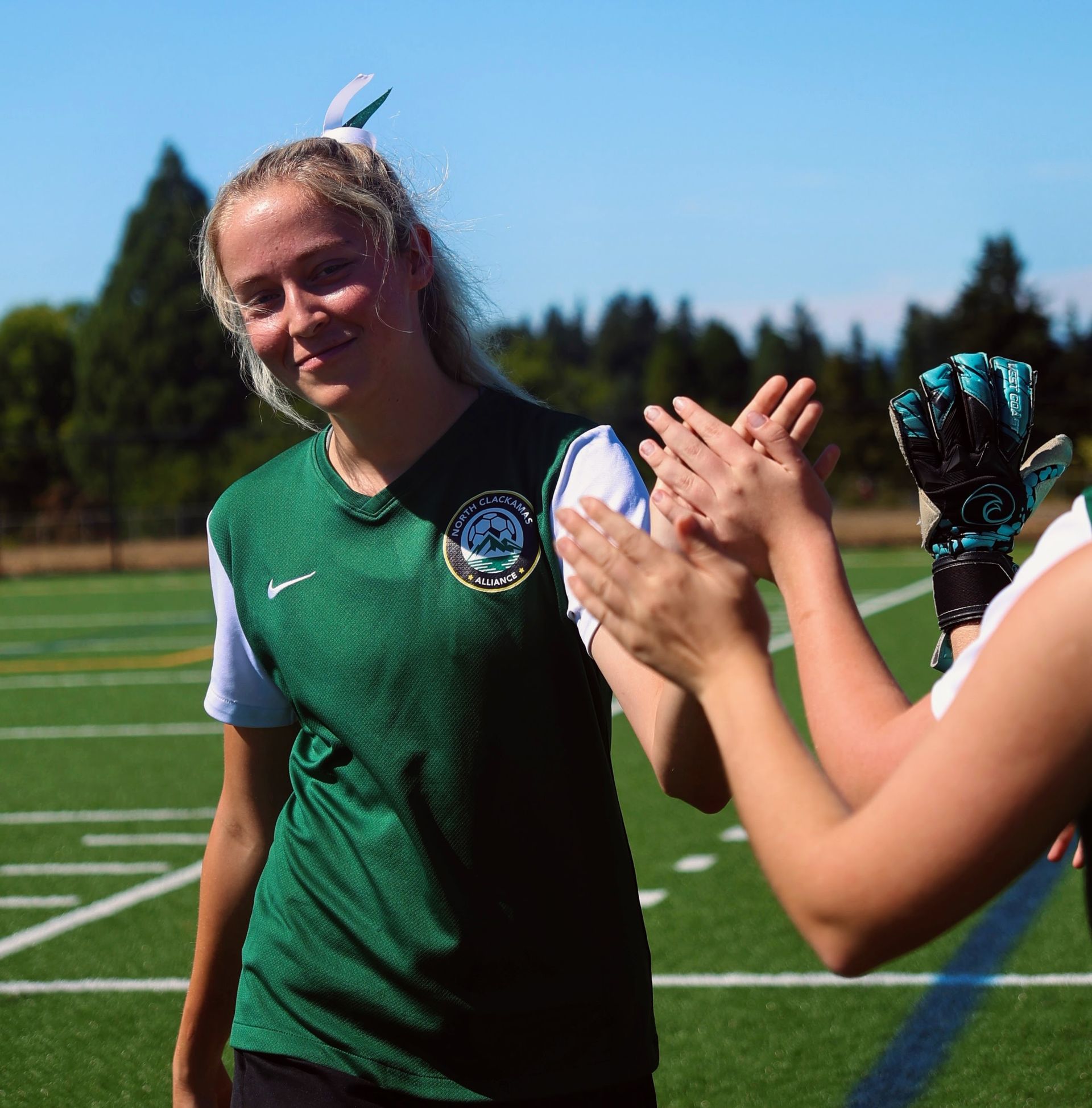 Soccer player in green jersey high-fiving teammate on a sunny field.