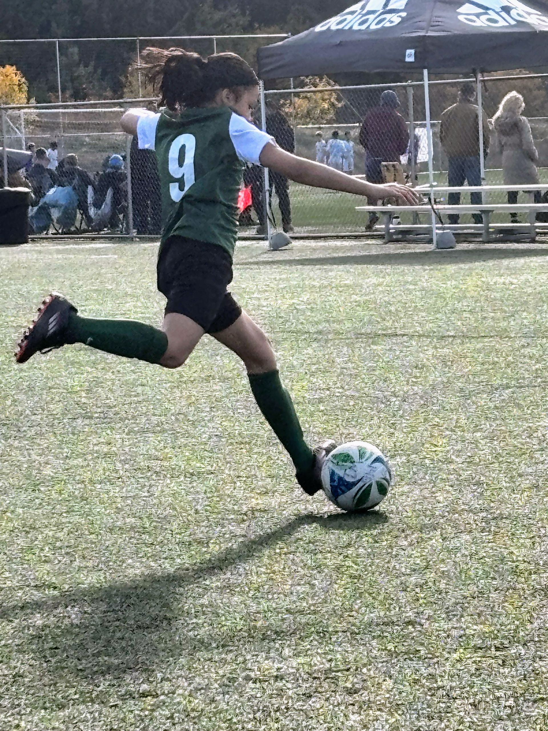 Soccer player in green jersey kicking ball on field.
