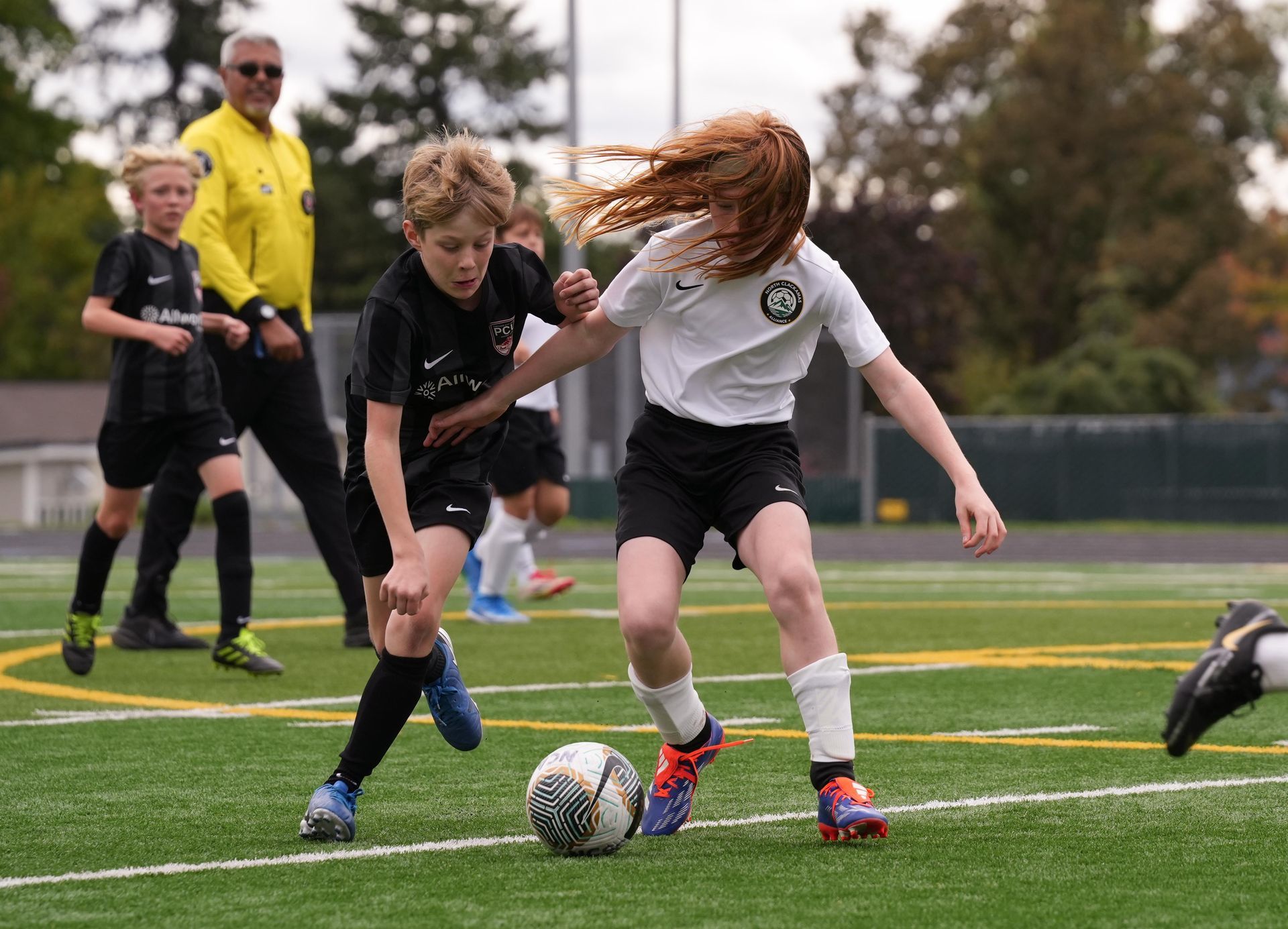 Soccer players in black and white uniforms compete for the ball on a green field. Referee watches.