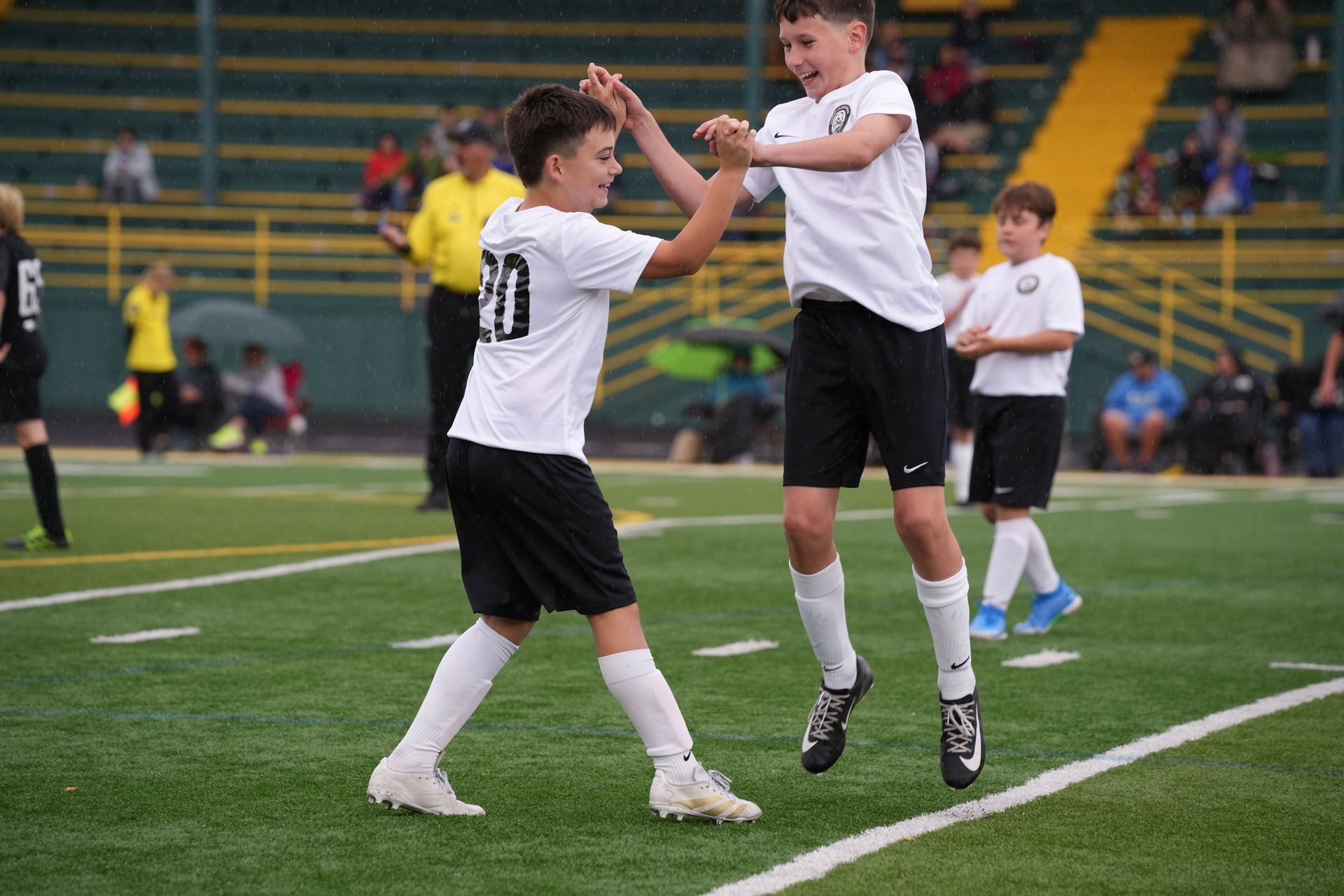 Two soccer players in white jerseys and black shorts high-fiving on a green field.