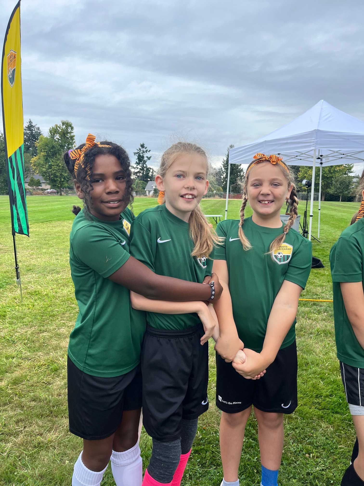 Three soccer players in green jerseys and black shorts stand on a field, smiling.