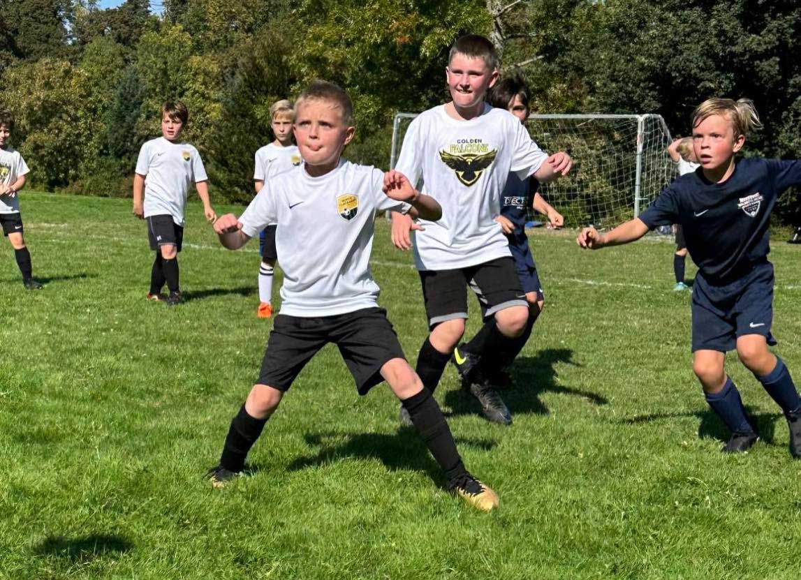 Kids playing soccer on a grassy field; two are in focus, one kicking, others running.