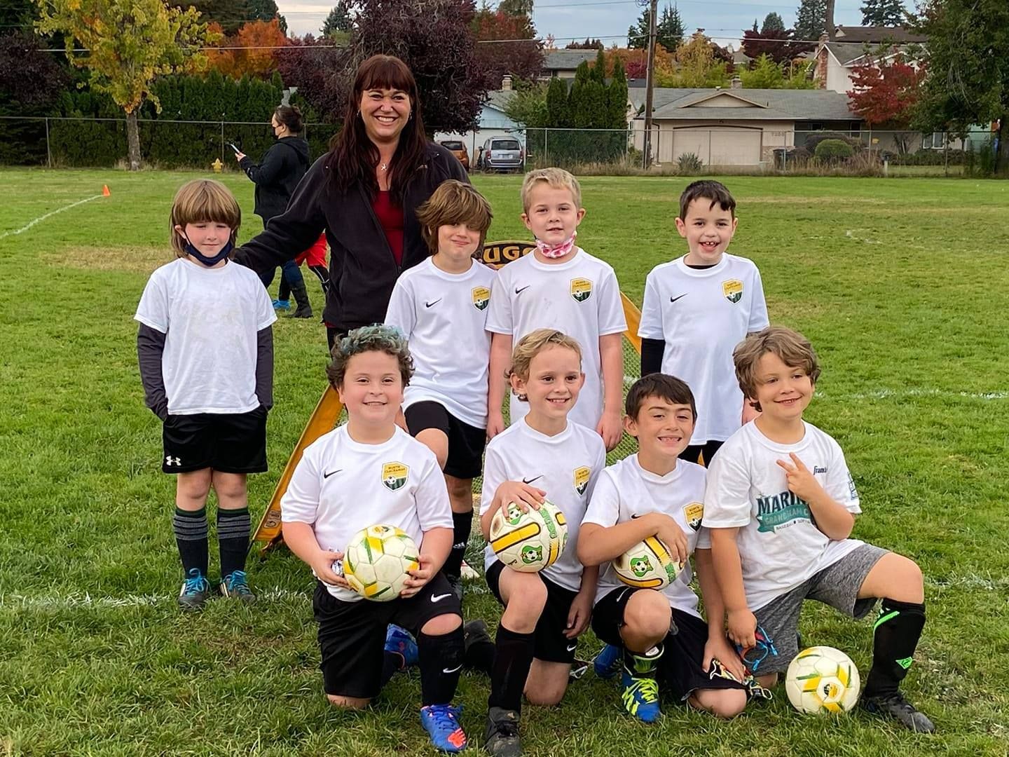 Youth soccer team posing on a grassy field with a female coach.