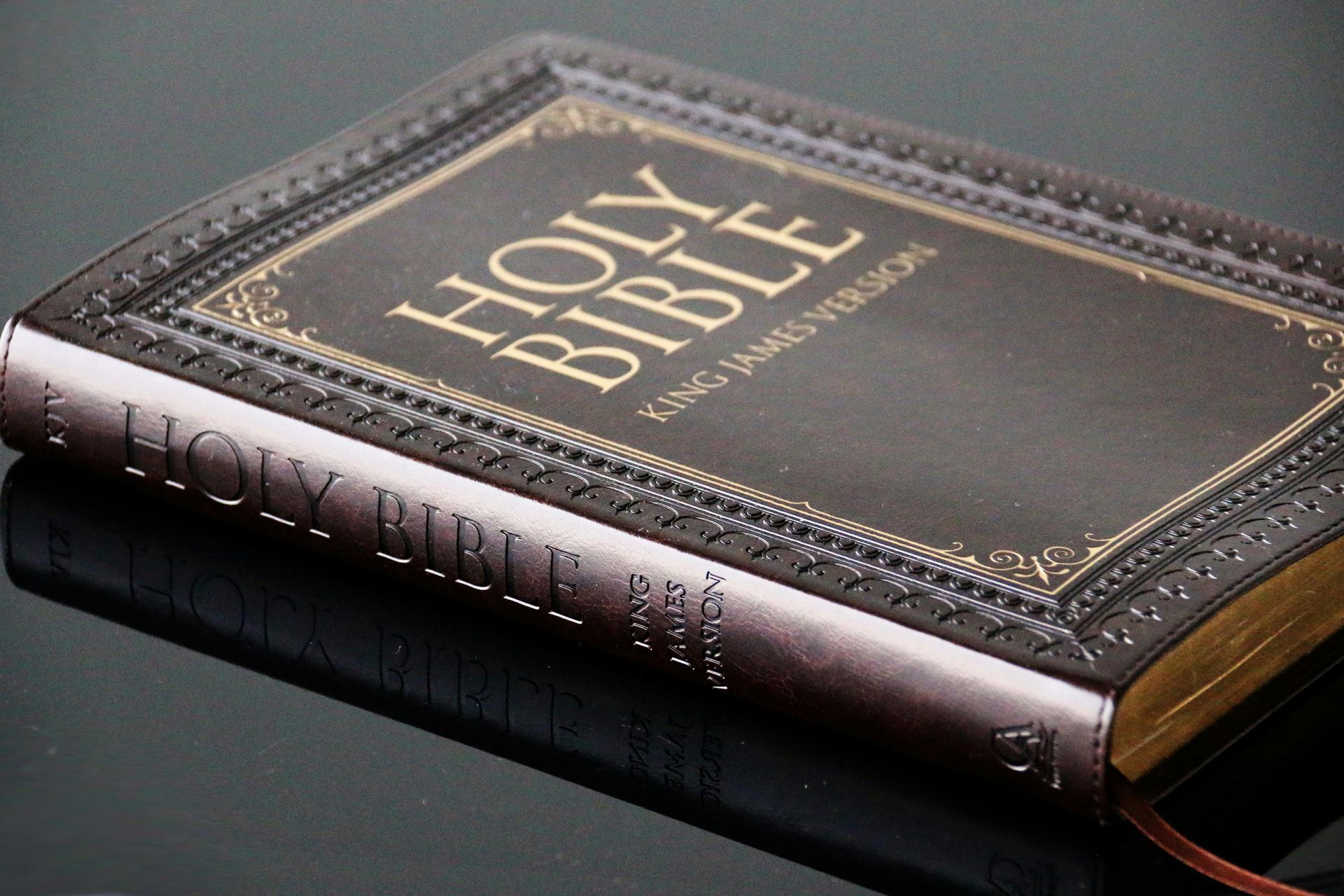 A leather-bound Holy Bible with gold lettering resting on a reflective, dark surface.