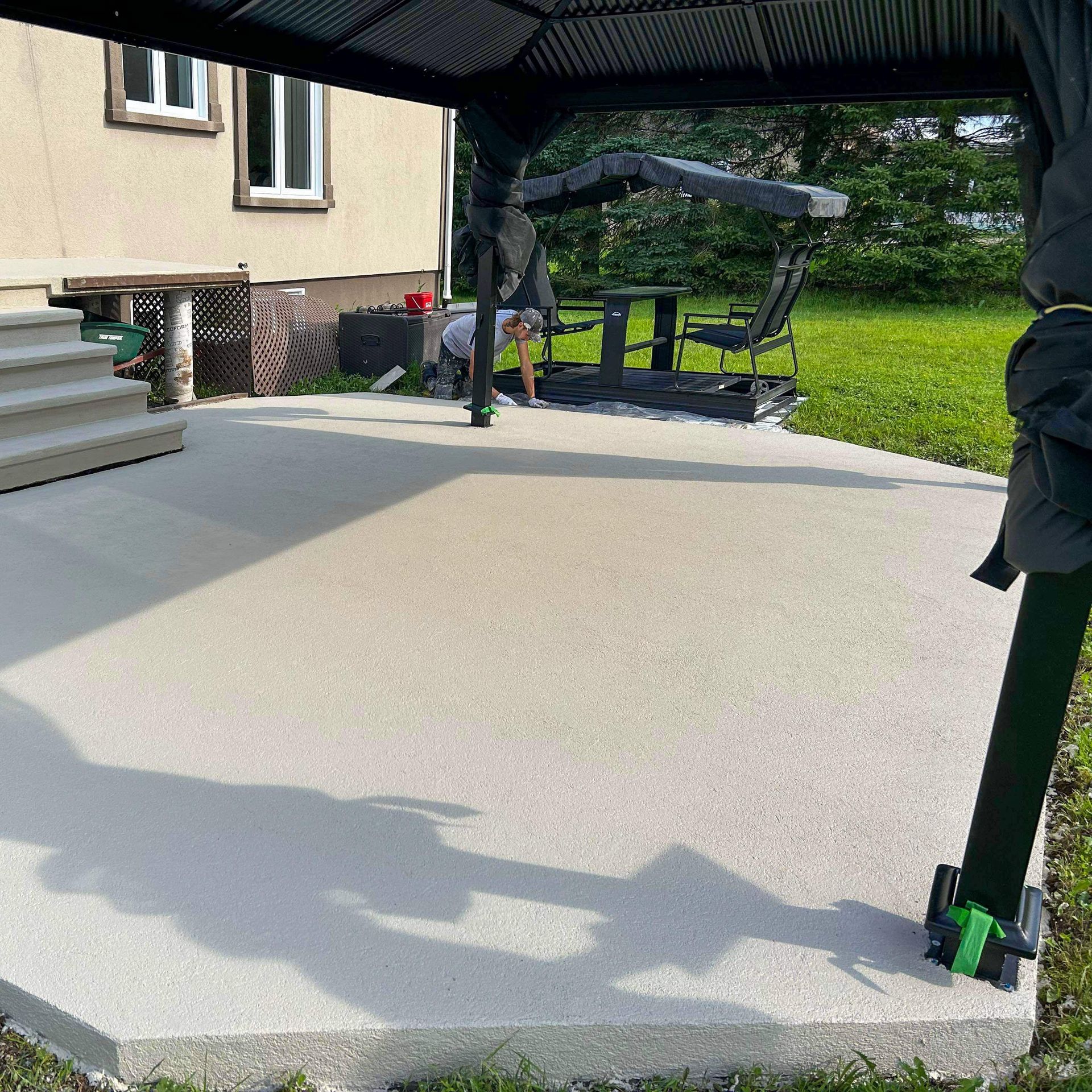Patio en béton avec gazebo et mobilier de jardin, situé à côté d'une maison et de gazon.