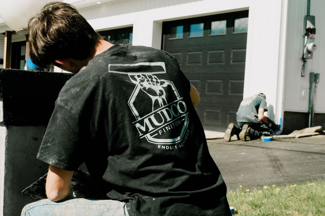 Un homme en chemise noire avec logo travaillant à l'extérieur ; une deuxième personne travaille également en arrière-plan.