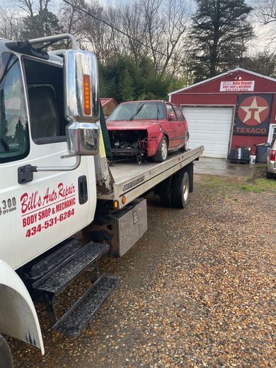A tow truck is carrying a red car on the back of it.