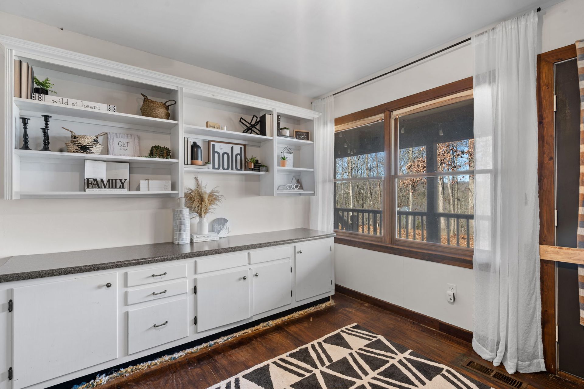 White cabinets and shelves in a room, with window showing trees outside. A rug is on the floor.