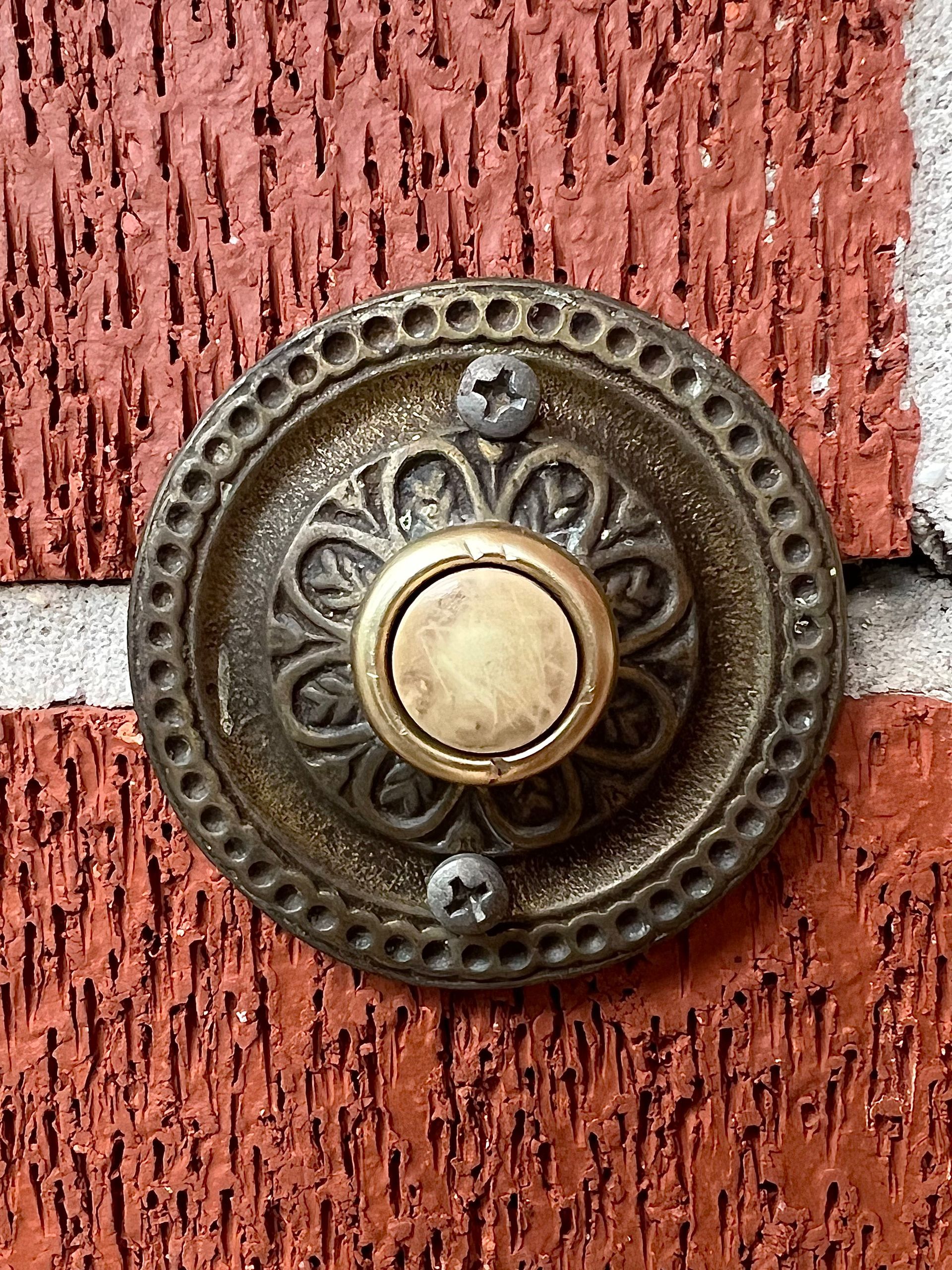 Ornate brass doorbell on a red brick wall.