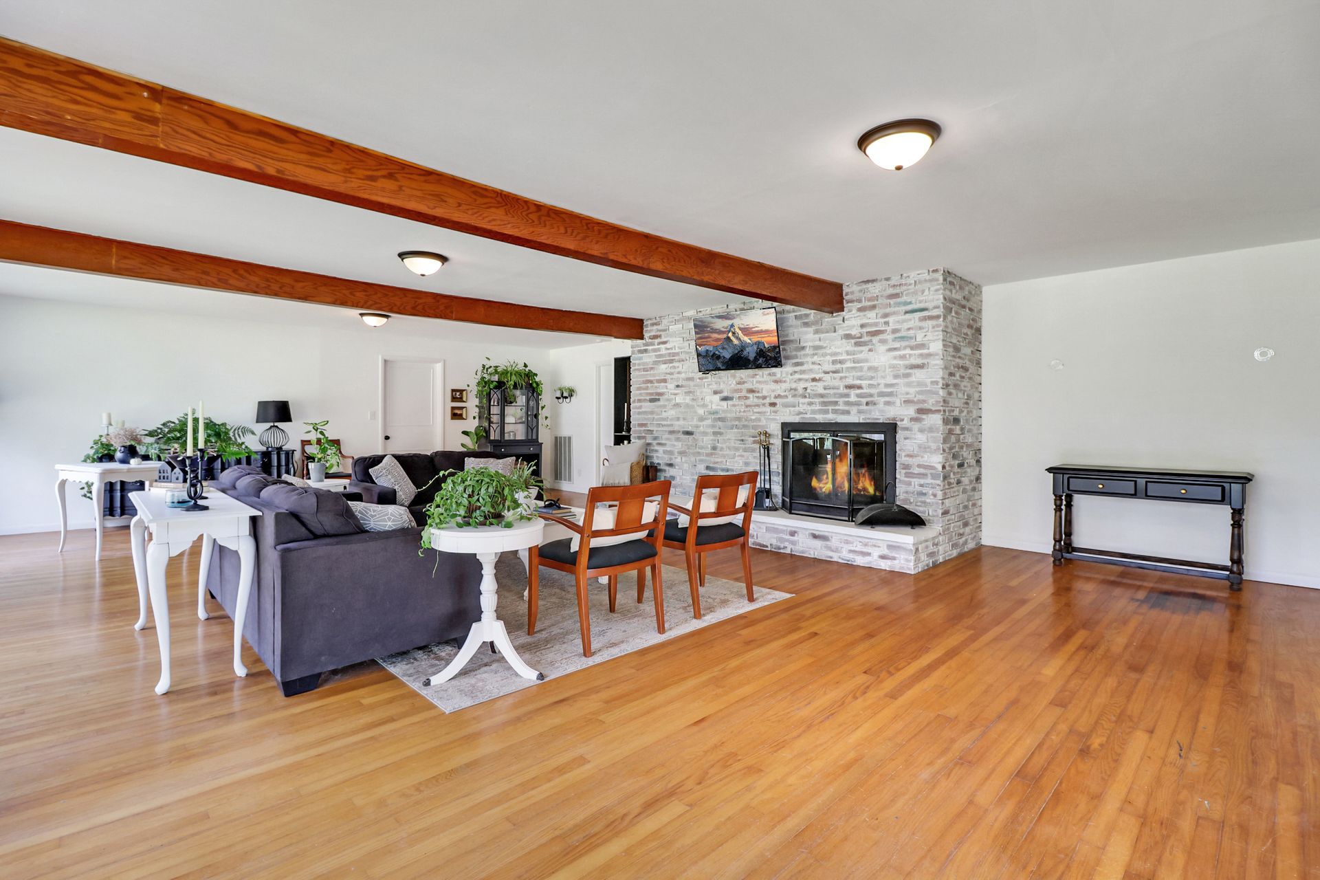 Spacious living room with hardwood floors, a fireplace, and exposed wooden beams.