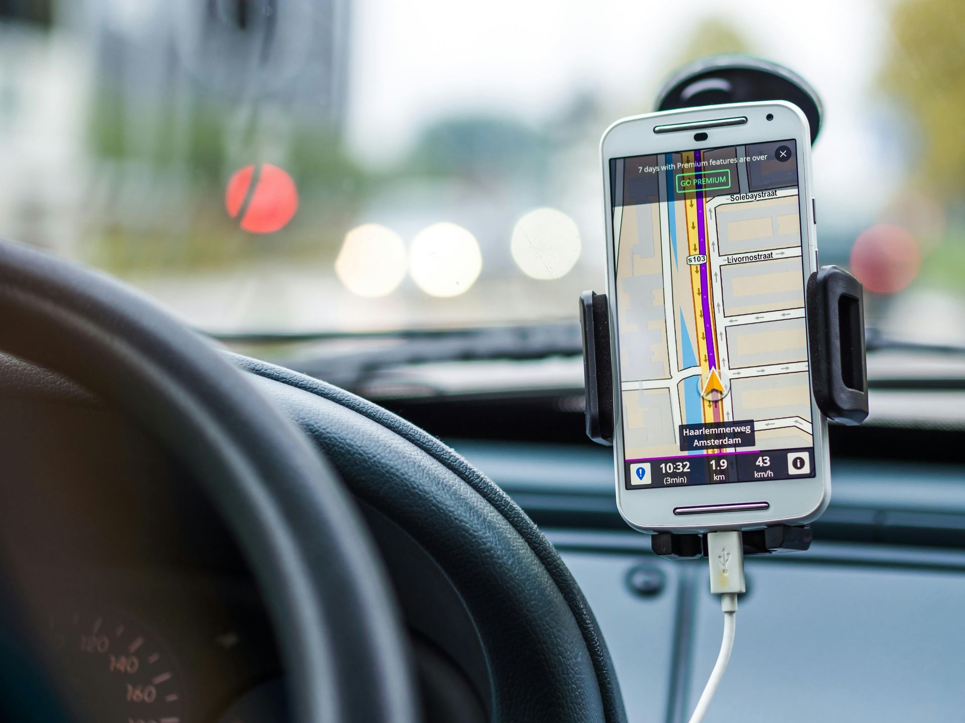 A smartphone with GPS directions mounted in a car. Dashboard and steering wheel are visible.