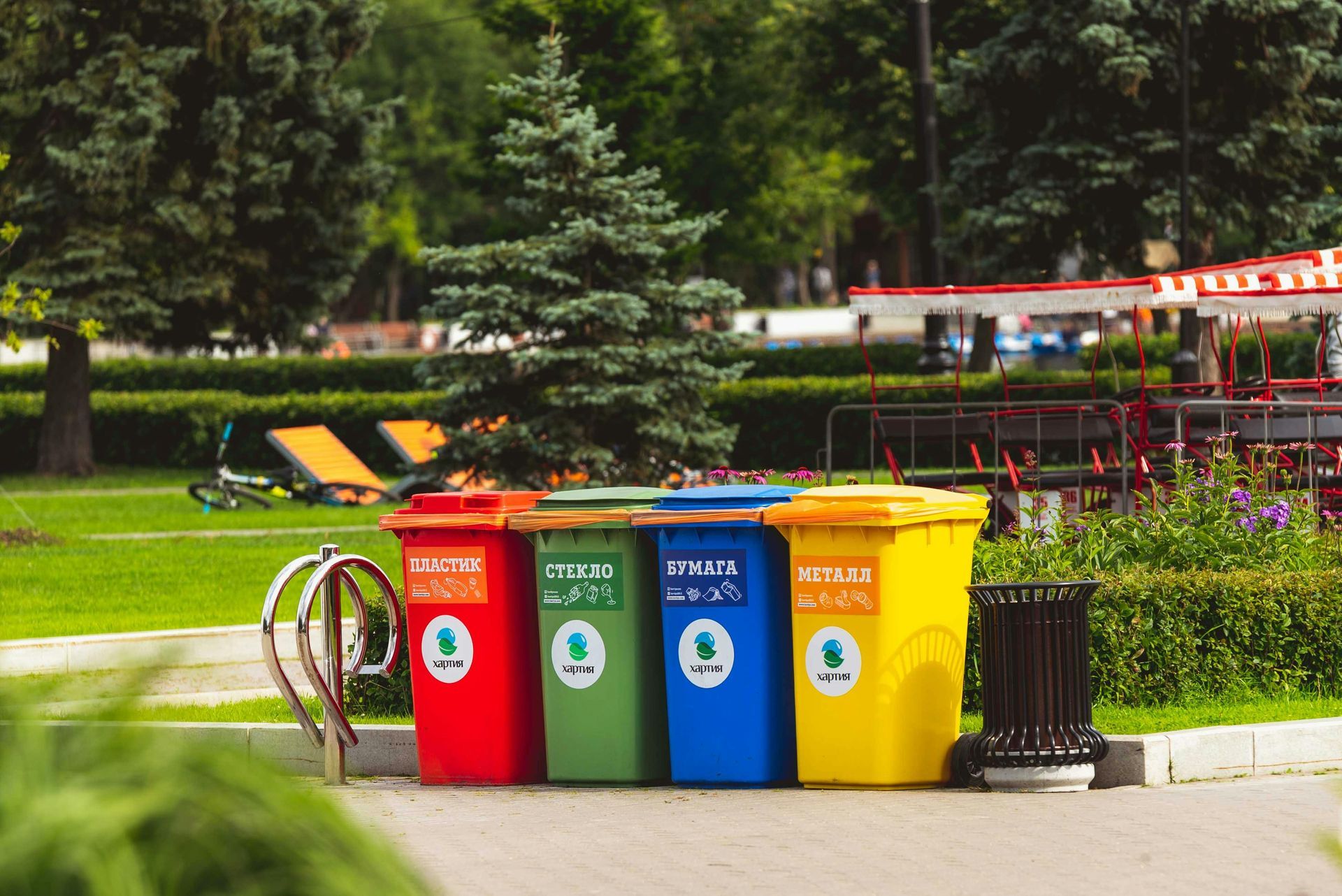 Four colorful recycling bins in a park: red, green, blue, and yellow.