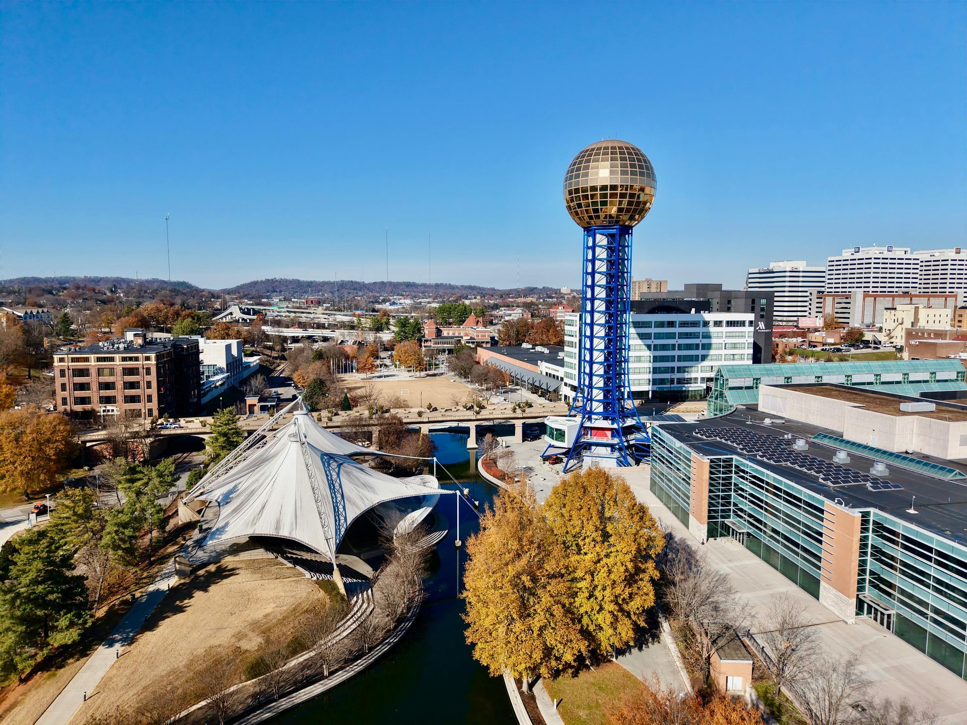 World's Fair Sunsphere in Knoxville, TN, with a blue tower and golden ball. Trees, buildings, and a canal visible.