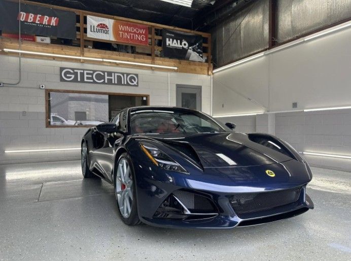 Dark blue sports car parked in a garage with GTECHNIQ signage on the wall.