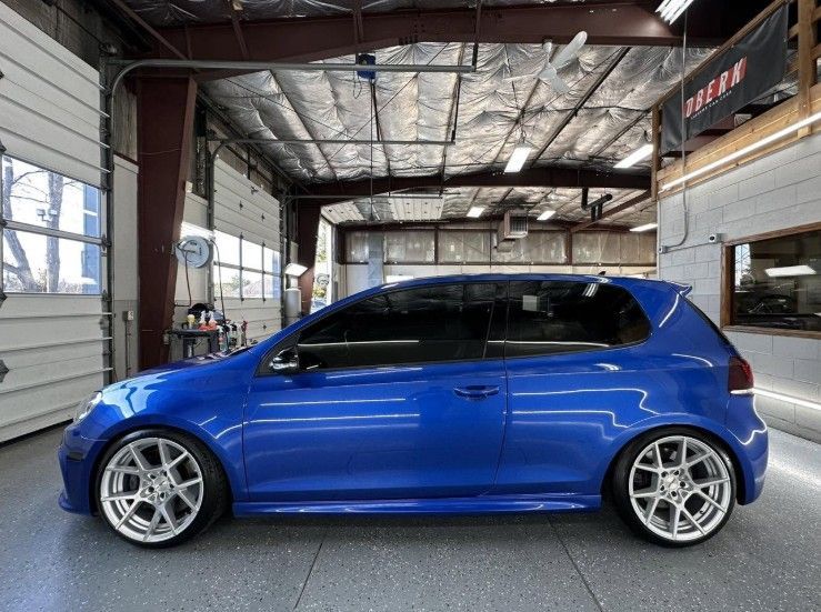 Blue hatchback car in a garage, side view with silver rims and tinted windows
