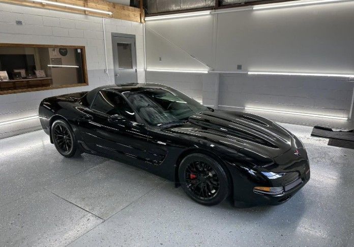 Black sports car parked in a modern garage with bright white walls and floor lighting