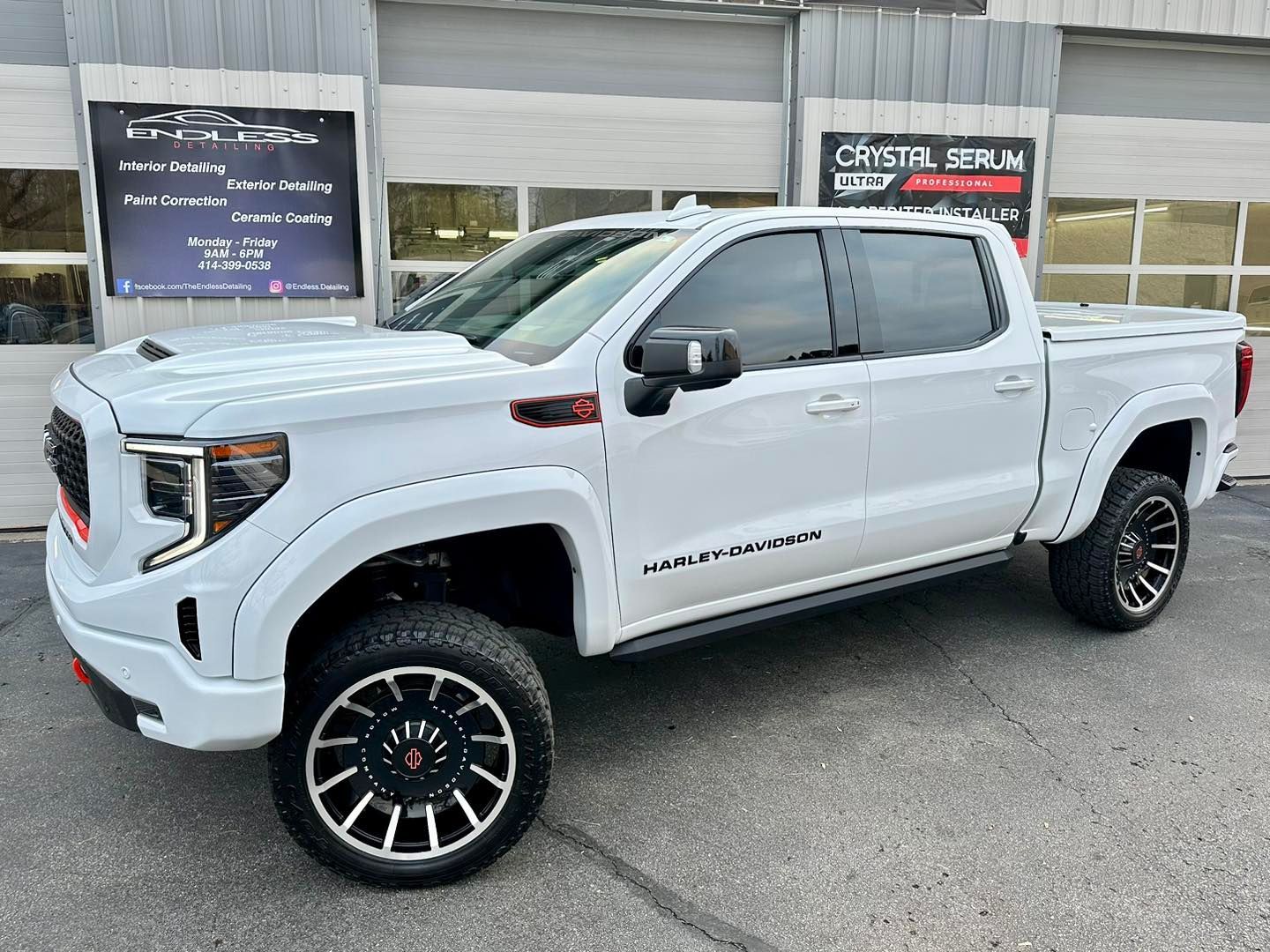 White GMC truck parked in front of a shop, custom wheels, tinted windows.