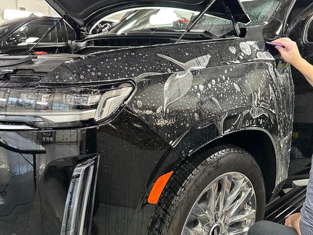 Black car being covered in clear protective film, inside a garage.