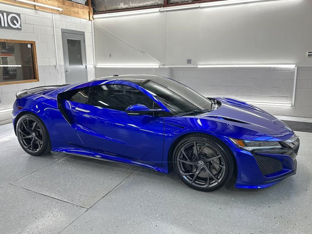 Blue Acura NSX sports car in a garage with gray flooring and bright lighting.