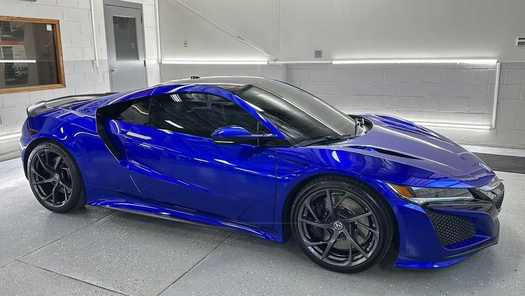 Blue Acura NSX sports car in a white garage, angled view.