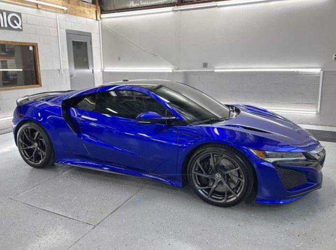 Blue sports car parked indoors in a garage with bright overhead lights.