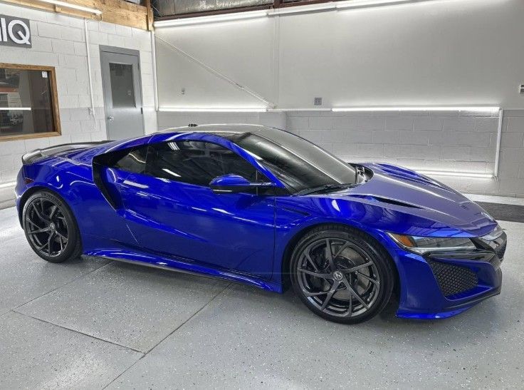 Blue sports car parked indoors in a garage, viewed from the side.