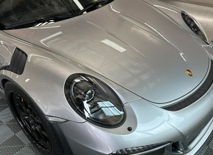 Silver Porsche sports car, close-up of the front. Headlights, black rims, and vents are visible.