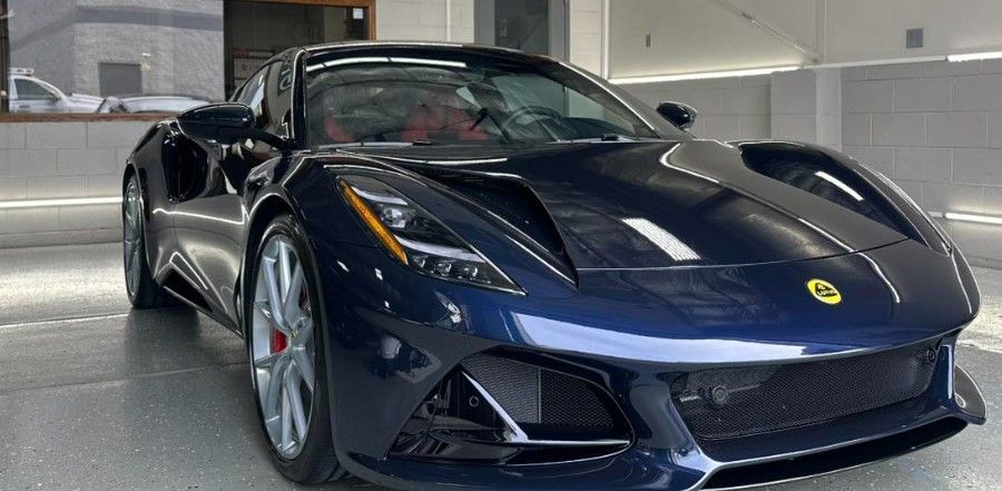 Dark blue sports car parked indoors under bright lights, front three-quarter view