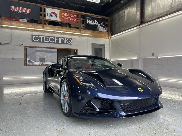 Dark blue sports car in a showroom with GTECHNIQ signage and polished floors