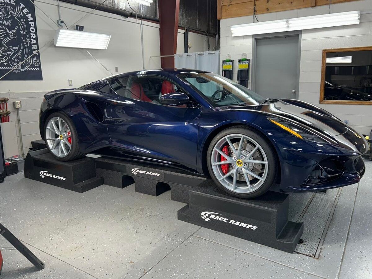 A blue sports car is parked on a set of ramps in a garage.