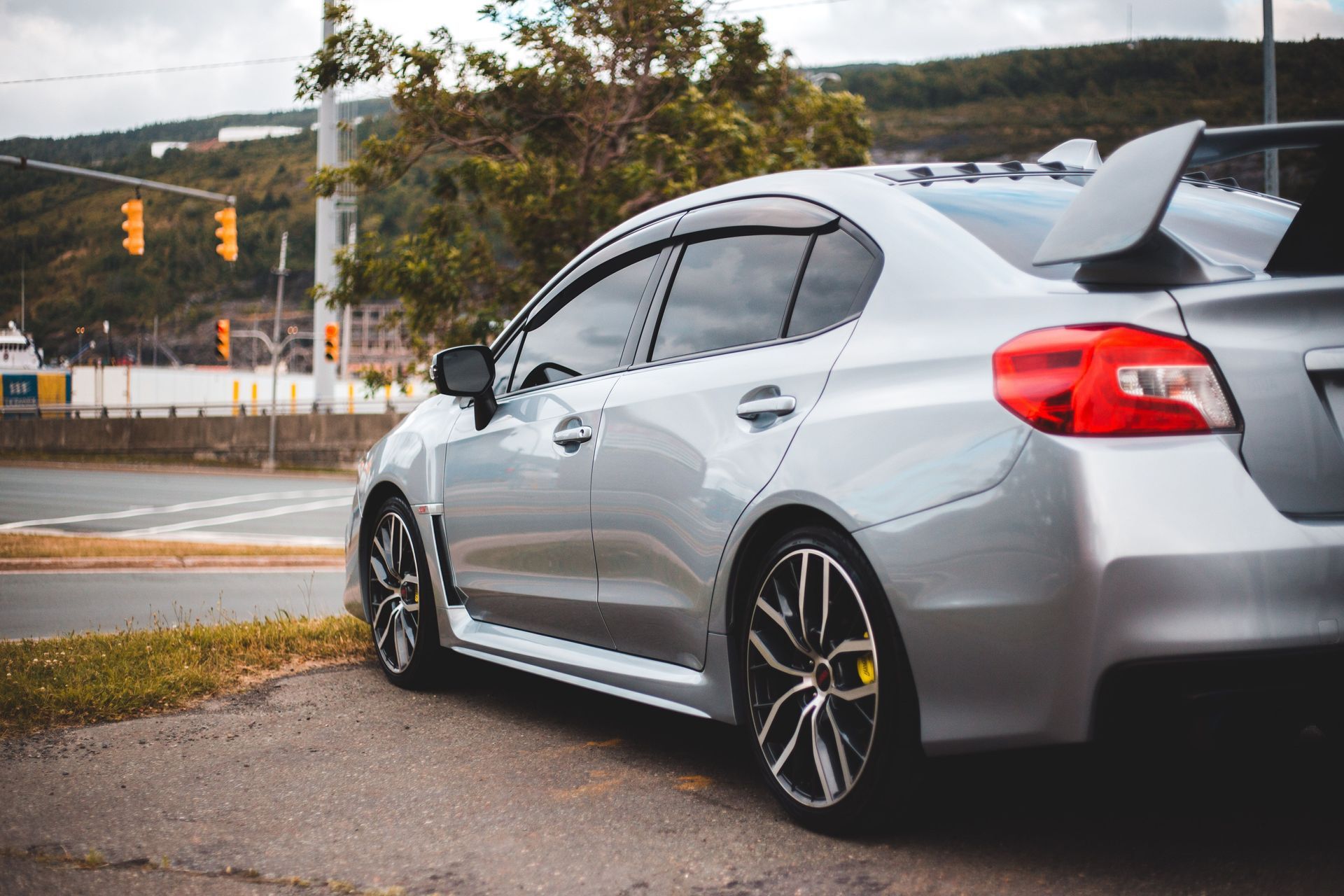 Silver hatchback parked beside a warehouse building under a cloudy sky.