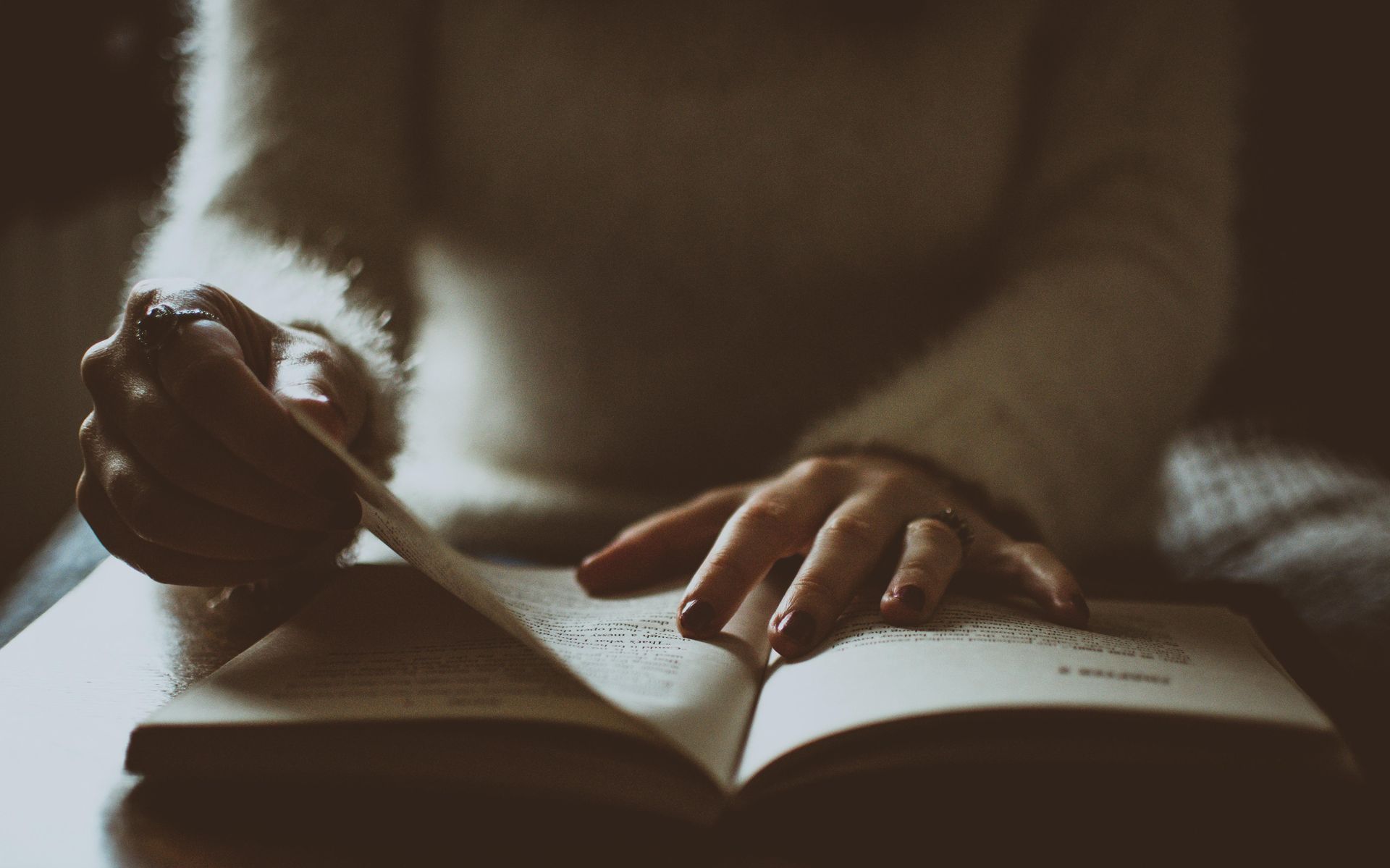 A woman is sitting at a table reading a book.