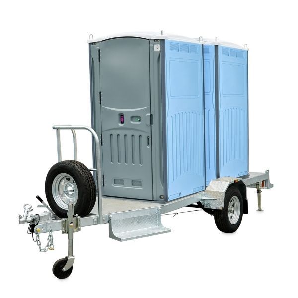 Portable restroom trailer, grey and blue units, on a trailer with a spare tire.