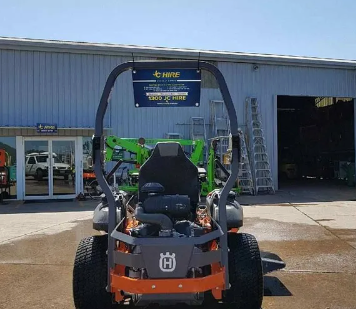 Orange and black zero-turn mower parked outside a shop with an open garage door