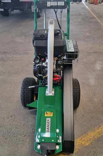 Green walking lawn mower shown from above in a workshop aisle, with large rear wheels and black engine.