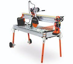 Wet tile saw, orange and silver, on folding legs. Blade spinning, water supply visible, ready for cutting.
