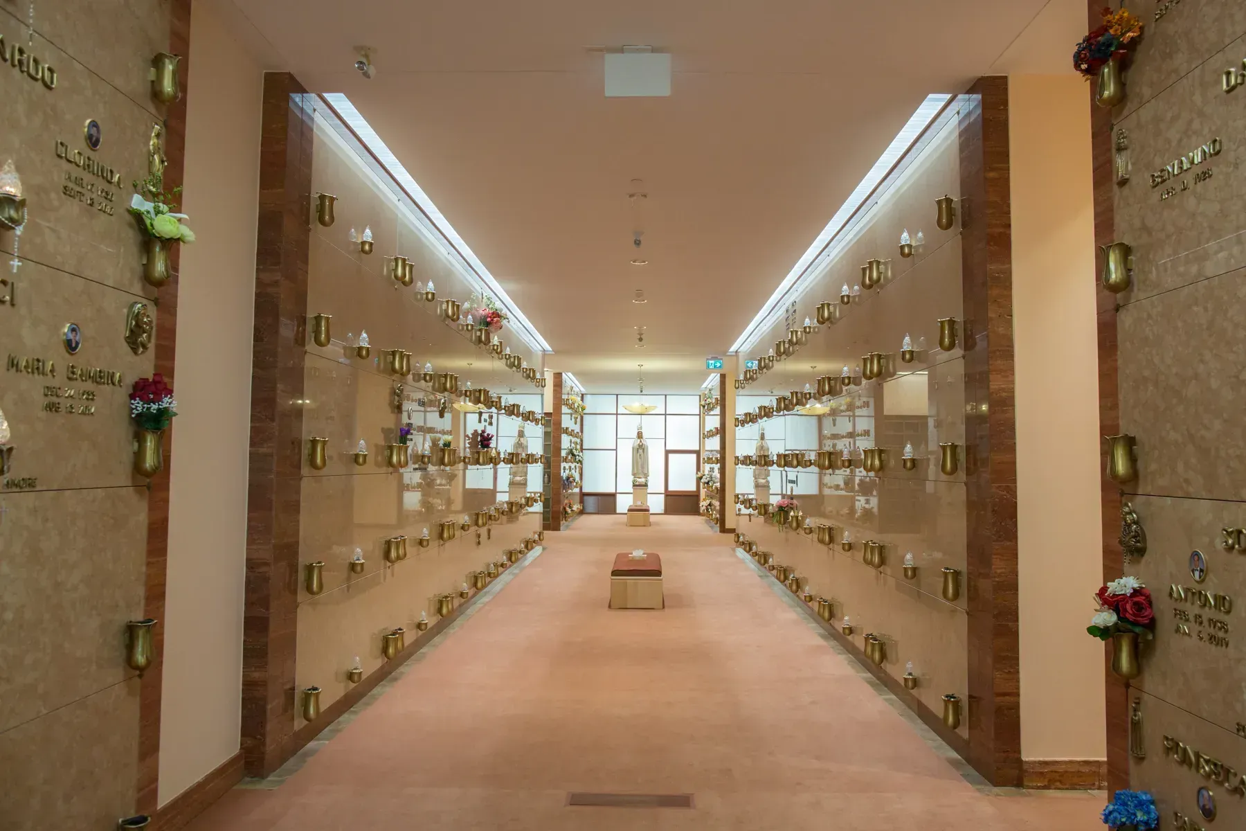 Long glass-walled memorial corridor with plaques and flowers on both sides