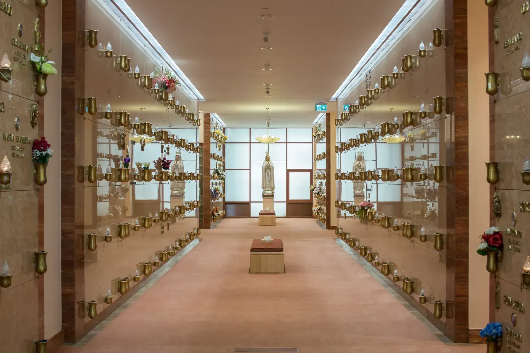 Long memorial columbarium corridor with rows of niches and flowers under warm lighting