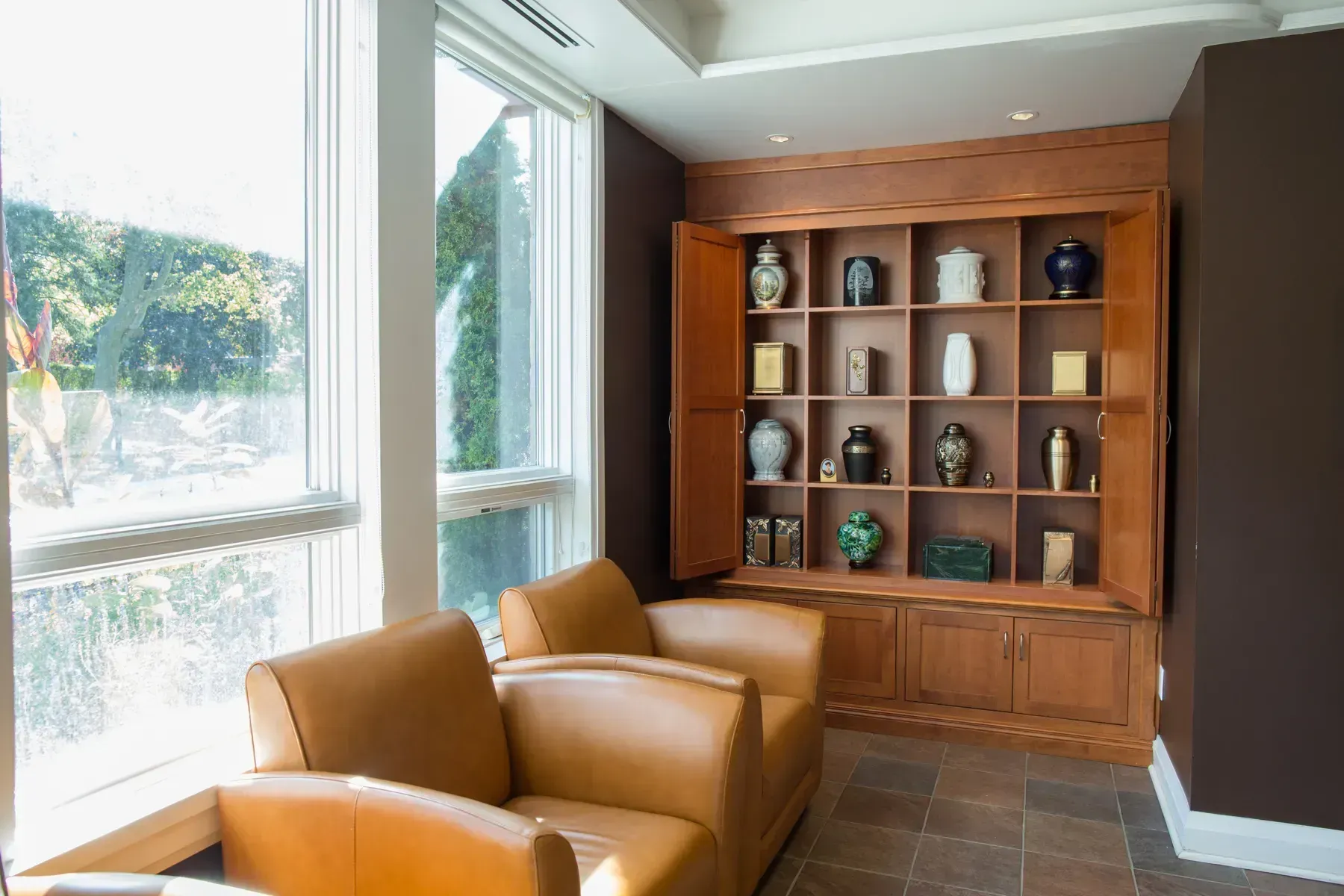 Sunlit lounge with tan chairs and a built-in wood bookshelf/display cabinet.