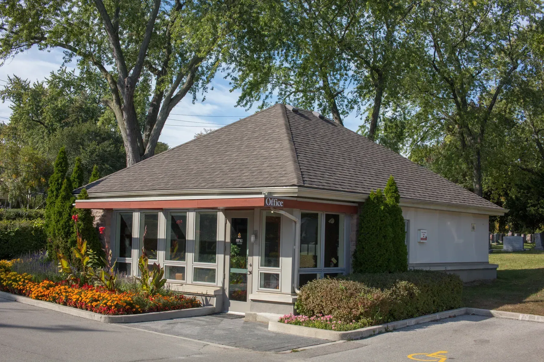 Small white building with a red awning, flower beds, and trees in front.