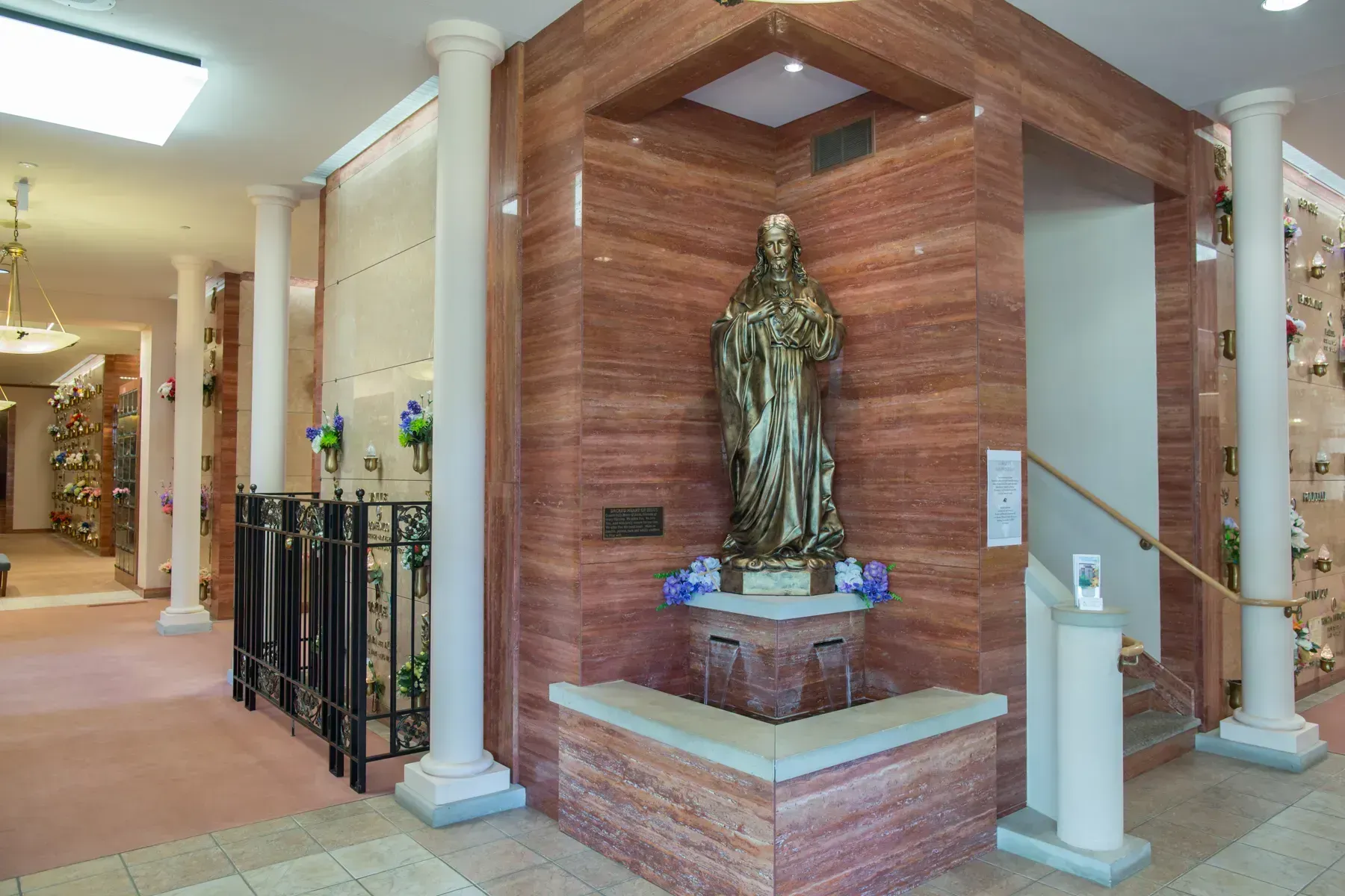Indoor hallway with columns and a robed statue on a brick pedestal
