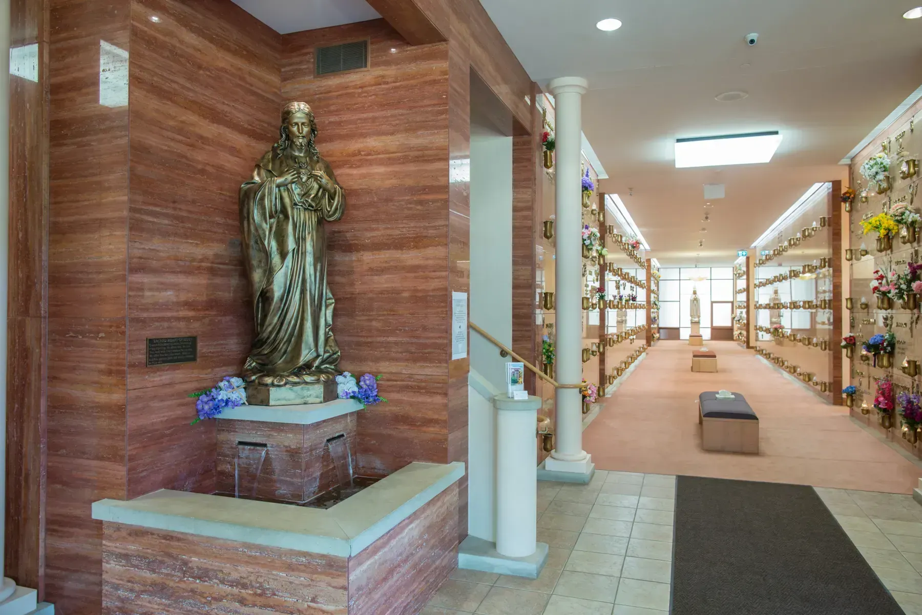 Indoor shrine with a statue in a wood-paneled alcove beside a lit corridor with shelves and benches